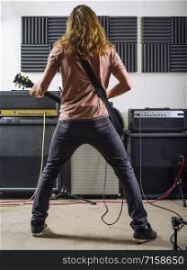 A young man with long hair playing electric guitar in a recording studio.