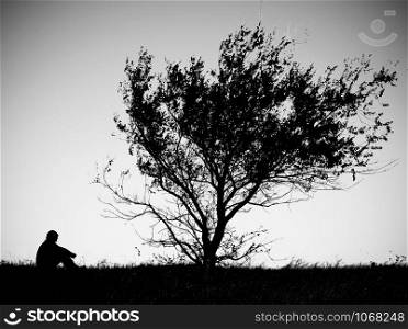 A young mas sitting on the grass under the tree. Black and white image of a man under the tree.