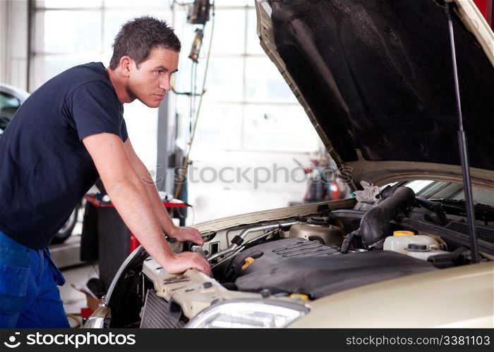 A young mechanic staring at a car, thinking