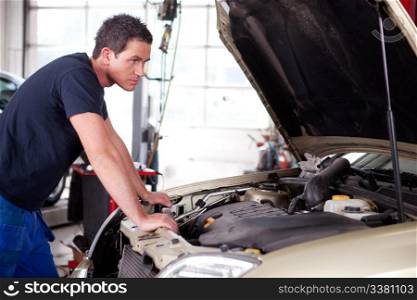 A young mechanic staring at a car, thinking