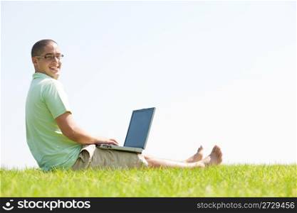 A young men sit on the grass in the park using a laptop