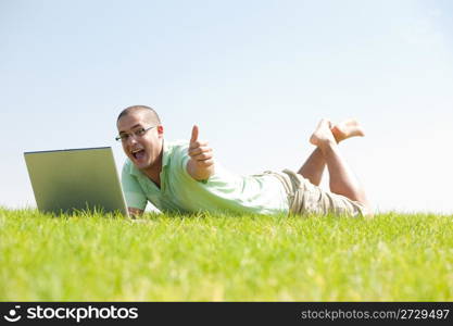 A young men sit on the grass in the park using a laptop