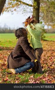 A young mixed race girl playing in the autumn leaves with her black mother