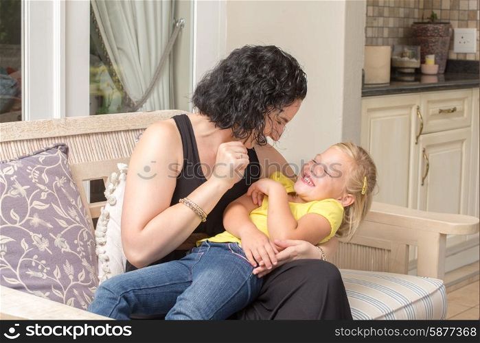 A young mother and her daughter are playing and having fun while sitting on a couch outside on the porch of their home.