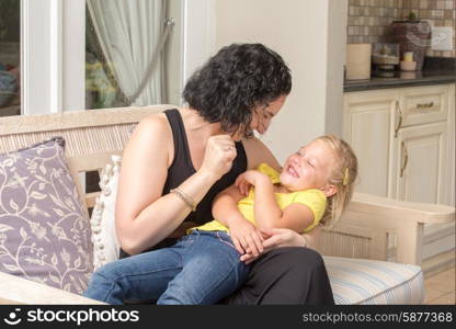 A young mother and her daughter are playing and having fun while sitting on a couch outside on the porch of their home.