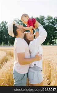 A young mother, father and little son enjoy nature together in the fresh air. A happy family with a child walks through a wheat field and enjoys the sweet moments of their life