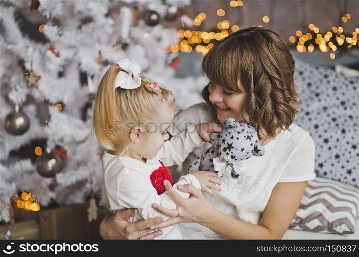 A young mother gently hugs the little girl before Christmas.. Family hug of a mother and daughter in front of a Christmas tree 7118.