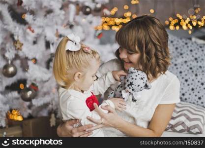A young mother gently hugs the little girl before Christmas.. Family hug of a mother and daughter in front of a Christmas tree 7118.