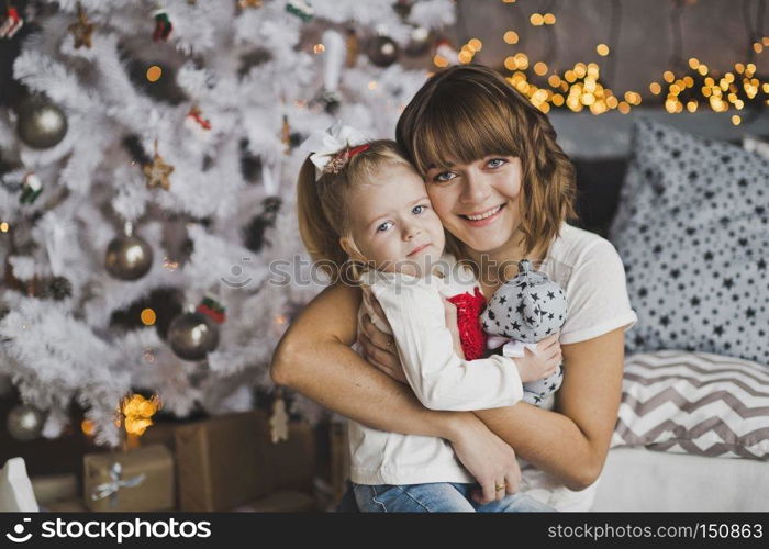 A young mother gently hugs the little girl before Christmas.. Family hug of a mother and daughter in front of a Christmas tree 7121.