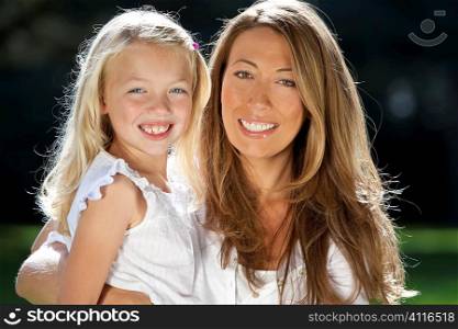 A young mother with hher blond daughter cuddling, smiling and having fun in a sun bathed green park