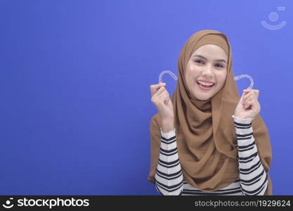 A young muslim woman holding invisalign braces in studio, dental healthcare and Orthodontic concept. . Young muslim woman holding invisalign braces in studio, dental healthcare and Orthodontic concept.