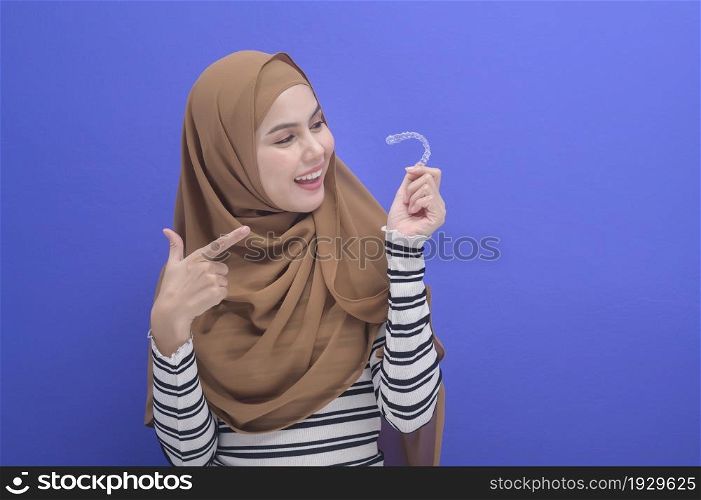 A young muslim woman holding invisalign braces in studio, dental healthcare and Orthodontic concept. . Young muslim woman holding invisalign braces in studio, dental healthcare and Orthodontic concept.