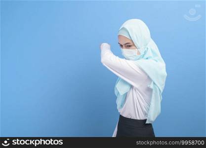 A young muslim woman with hijab wearing a surgical mask feeling sick and coughing over blue background studio.  . Young muslim woman with hijab wearing a surgical mask feeling sick and coughing over blue background studio.  