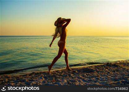 a young naked girl in one hat hat happily runs along a deserted sea beach