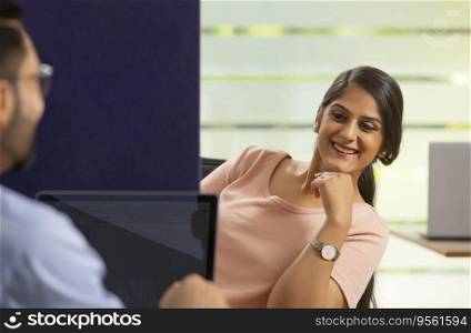 A YOUNG OFFICE EXECUTIVE COMFORTABLY SITTING WHILE LISTENING TO HER COLLEAGUE