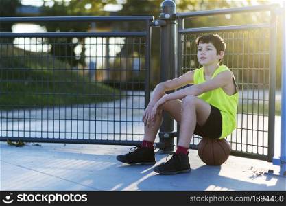 A young outdoors sitting on basket ball at a street court with ball. young outdoors sitting on basket ball at a street court with ball