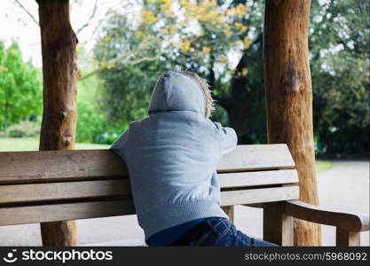 A young person wearing a hooded top is sitting in a shelter in the park