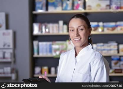 A Young pharmacist standing next to medicine shelves, holding tablet. Young pharmacist standing next to medicine shelves, holding tablet