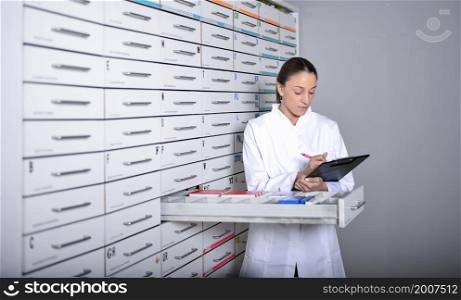 A Young pharmacist standing next to medicine shelves, holding tablet. Young pharmacist standing next to medicine shelves, holding tablet