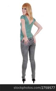 A young pretty and tall woman in jeans and green sweater standing from the back in the studio, holding her butt, over white background.