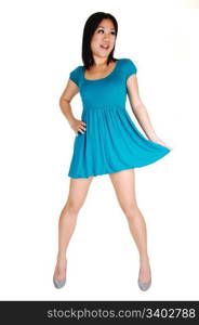 A young pretty Asian woman in a light blue short dress and high heelsstanding in the studio, pulling on her dress, for white background.