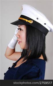 A young pretty Asian woman, in a sailor uniform and white gloves and sailor a cap , in an portrait, standing saluting in the studio for light gray background.