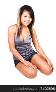 A young pretty Asian woman, in shorts and s silver gray top, sitting on thefloor in the studio and smiling in the camera, on white background.