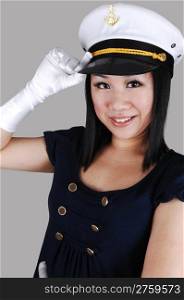 A young pretty Asian woman with cloves with a sailors cap,navy blue shirt, saluting over light gray background.