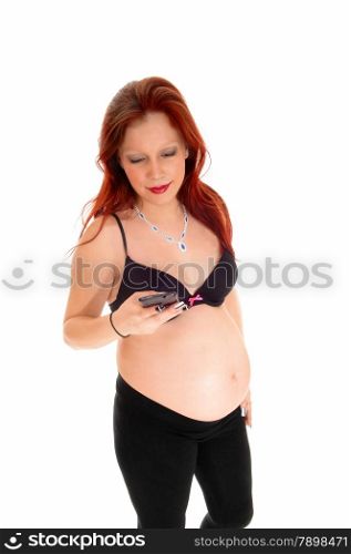 A young pretty pregnant women in a black bra and tights standing forwhite background, talking on her cell phone.