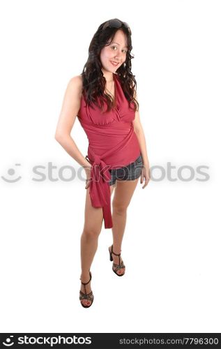 A young pretty woman in a red top and jeans shorts with long curlyblack hair standing for white background in the studio.