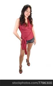 A young pretty woman in a red top and jeans shorts with long curlyblack hair standing for white background in the studio.