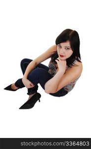 A young pretty woman in jeans and high heels sitting on thefloor of a studio, looking up into the camera, on white background.