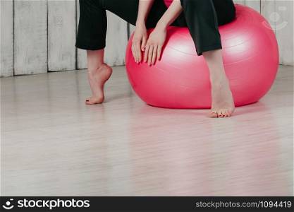 a young pretty woman sitting on a pink fitball in a gym, light floor and background, copy space