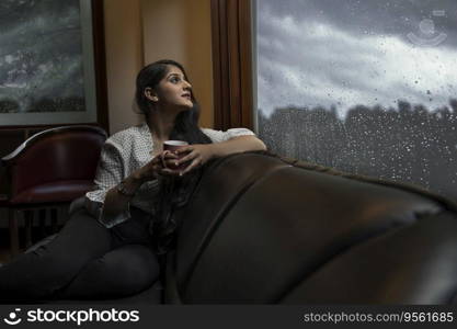 A YOUNG PROFESSIONAL RESTING ON SOFA AND LOOKING OUTSIDE ON A RAINY EVENING
