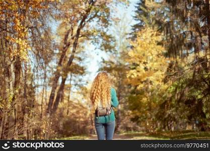 A young red-haired woman walks through the autumn park. A girl with lush curly hair looks at the autumn forest