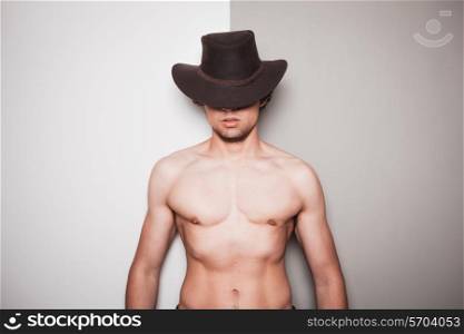 A young shirtless man wearing a cowboy hat is standing against a green and white beackground