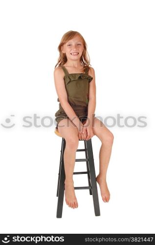 A young smiling blond girl in a olive green jumpsuit sitting in a bare chair,Isolated on white background.