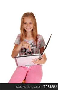A young smiling blond girl sitting in a pink pants, holding her folderand pointing at her work, isolated for white background.