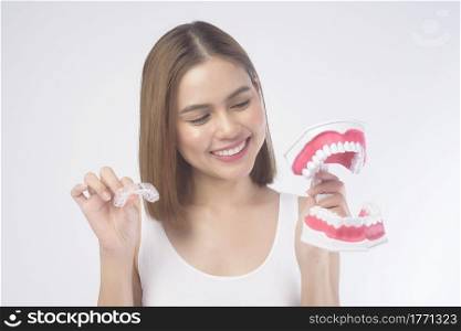A young smiling woman holding invisalign braces and artificial Dental Model over white background studio, dental healthcare and Orthodontic concept.. Young smiling woman holding invisalign braces and artificial Dental Model over white background studio, dental healthcare and Orthodontic concept.