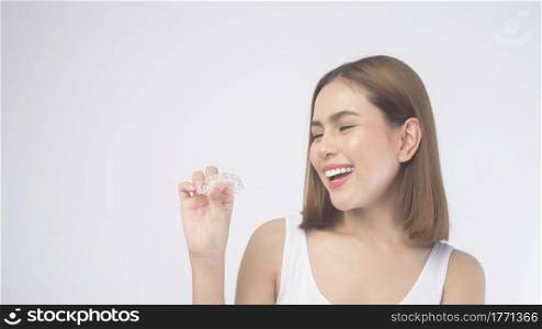 A young smiling woman holding invisalign braces over white background studio, dental healthcare and Orthodontic concept.. Young smiling woman holding invisalign braces over white background studio, dental healthcare and Orthodontic concept.