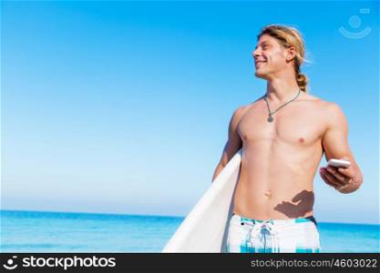 A young surfer on the beach with his mobile. Hello from the beach