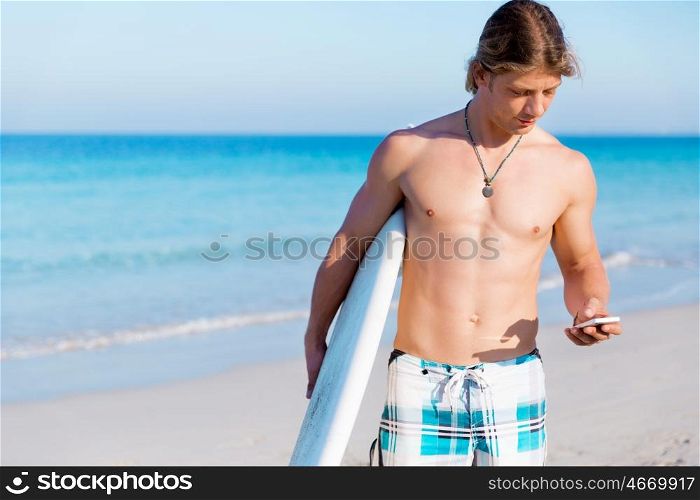 A young surfer on the beach with his mobile. Hello from the beach