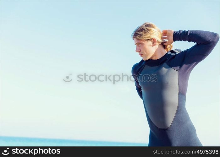 A young surfer putting on his wetsuit on the beach. Getting ready for a wave ride