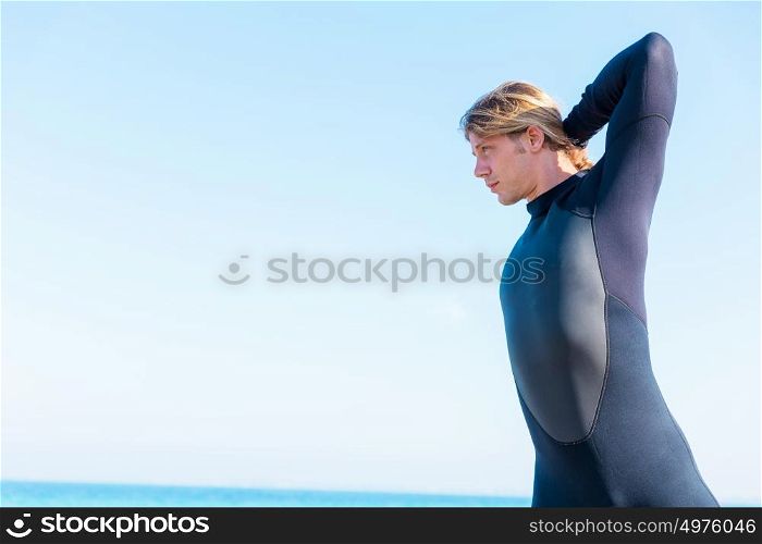 A young surfer putting on his wetsuit on the beach. Getting ready for a wave ride