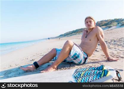 A young surfer with his board on the beach. Few minutes of rest