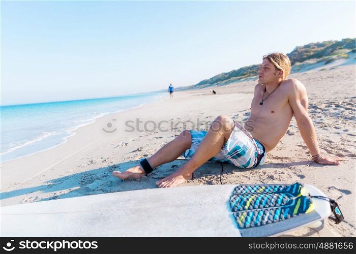 A young surfer with his board on the beach. Few minutes of rest