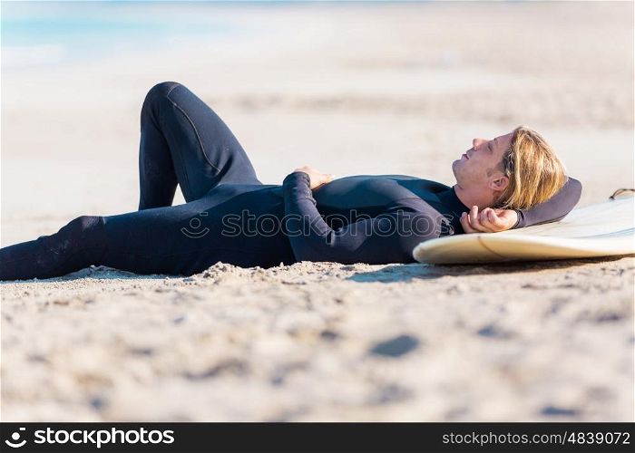 A young surfer with his board on the beach. I need some rest