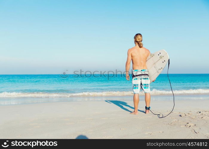 A young surfer with his board on the beach. Ready to hit waves