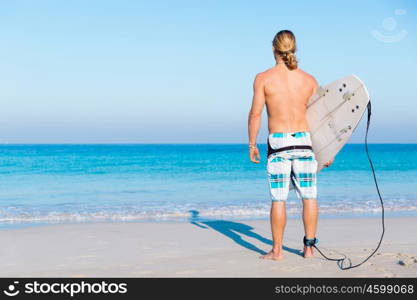 A young surfer with his board on the beach. Ready to hit waves