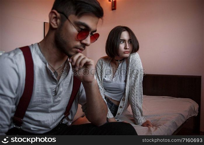a young swarthy guy and a young brunette girl are sitting on the bed in the bedroom with sad faces. selective focus on the girl